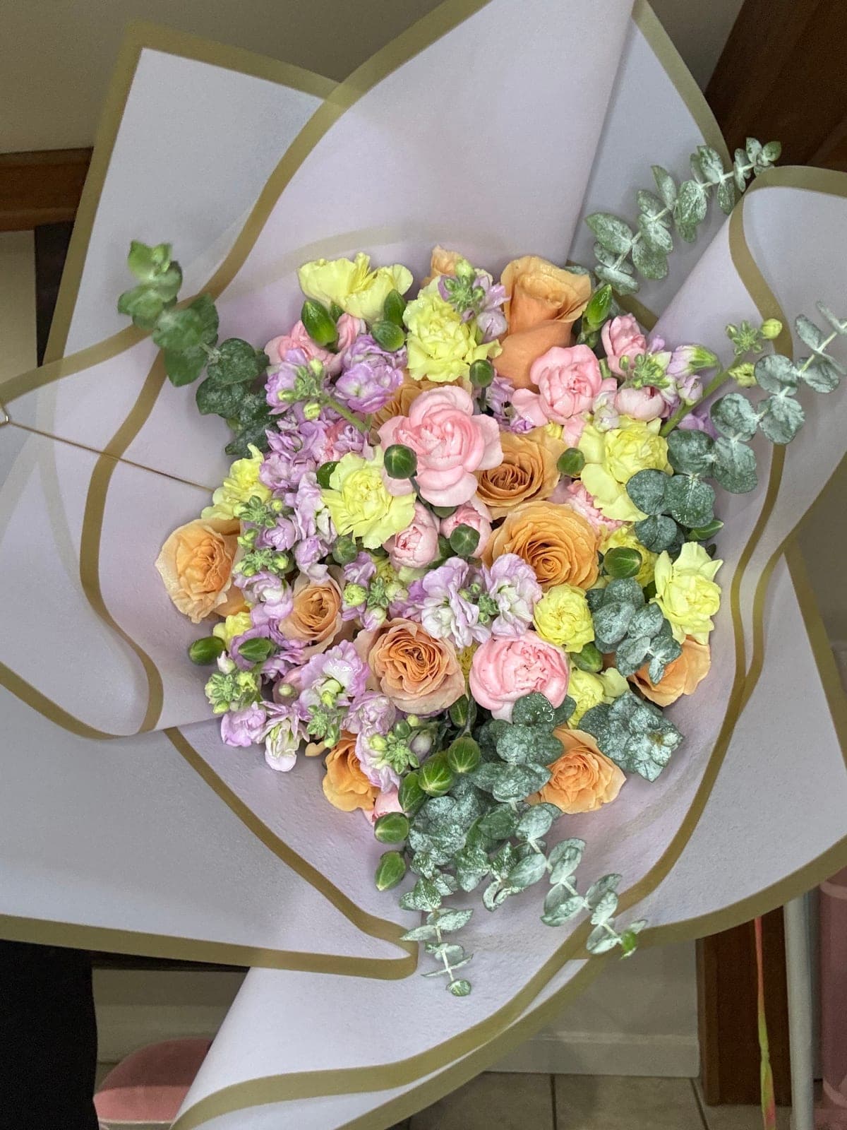 Wrapped custom bouquet of peach roses, pink and yellow carnations, lavender stock and eucalyptus