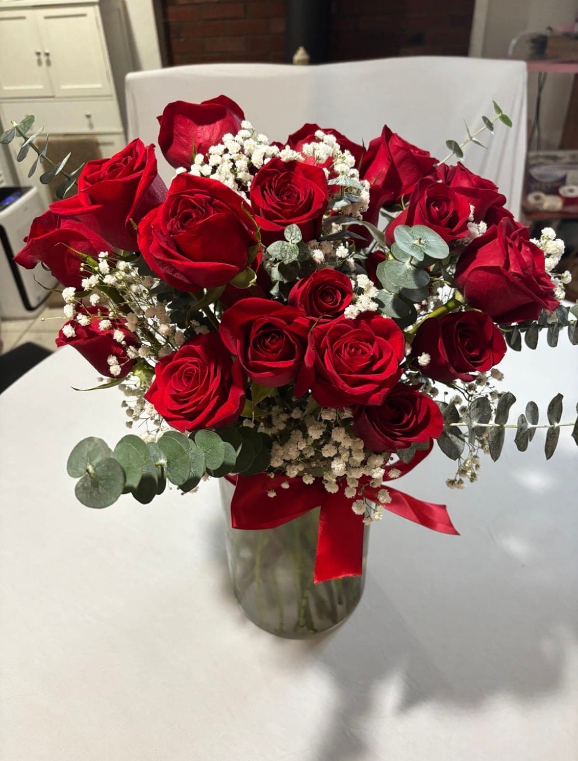 Red rose arrangement with baby’s breath and eucalyptus in a glass vase tied with a red ribbon