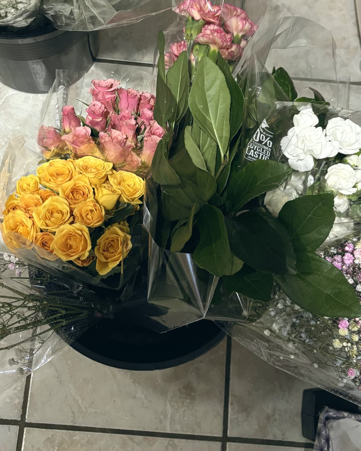 Yellow roses, pink spray roses, white carnations, baby’s breath and greenery still in their sleeves after delivery